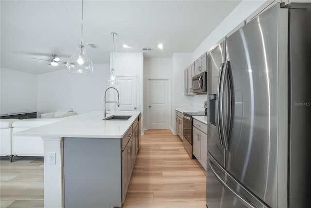 kitchen featuring light wood-type flooring, sink, stainless steel appliances, a center island with sink, and decorative light fixtures