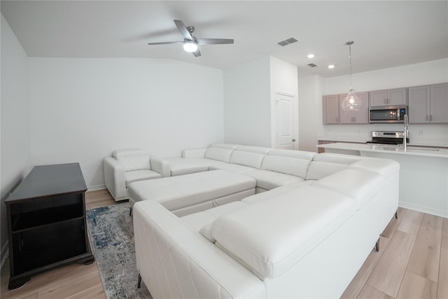 living room with ceiling fan, vaulted ceiling, and light hardwood / wood-style floors