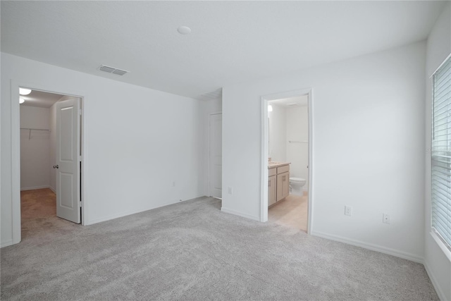 unfurnished bedroom with light carpet, a closet, ensuite bathroom, and a spacious closet