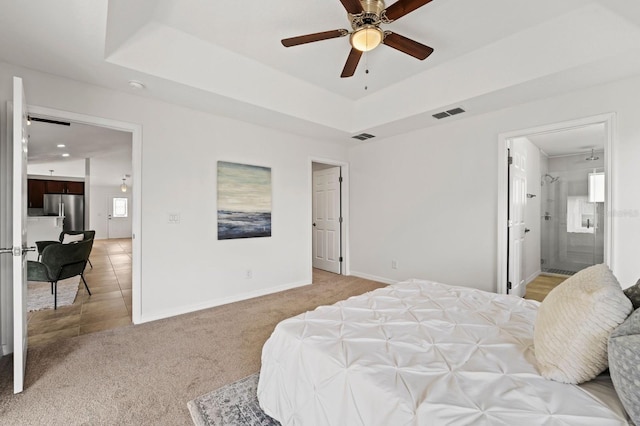 bedroom featuring stainless steel fridge, ensuite bath, light colored carpet, a raised ceiling, and ceiling fan