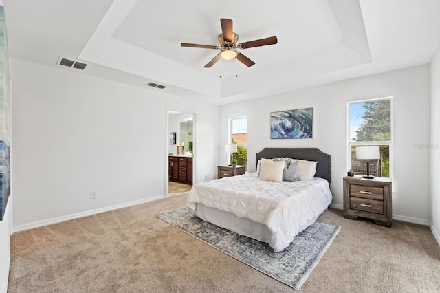 bedroom featuring ceiling fan, multiple windows, ensuite bathroom, and a tray ceiling