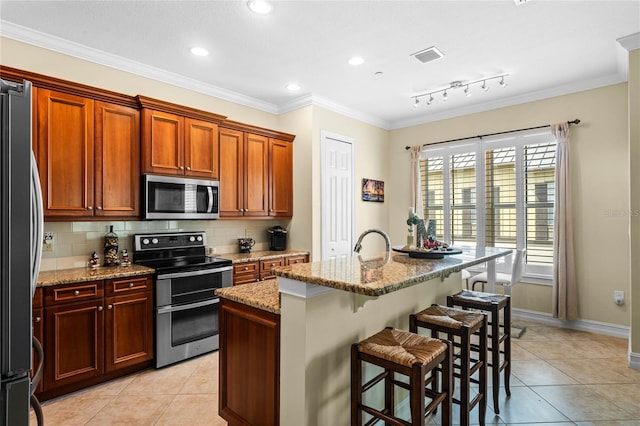 kitchen with light tile patterned floors, appliances with stainless steel finishes, light stone counters, and an island with sink