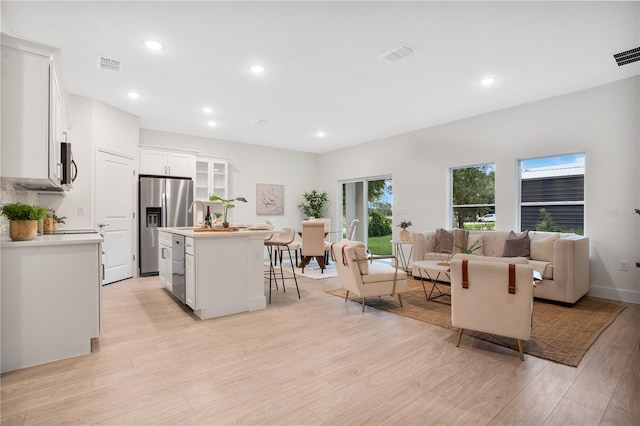 kitchen featuring an island with sink, a kitchen bar, stainless steel appliances, light wood-type flooring, and white cabinets