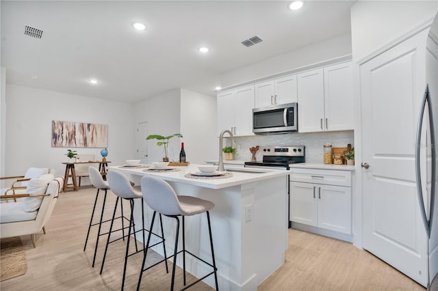 kitchen with a center island with sink, stainless steel appliances, white cabinets, and light hardwood / wood-style floors