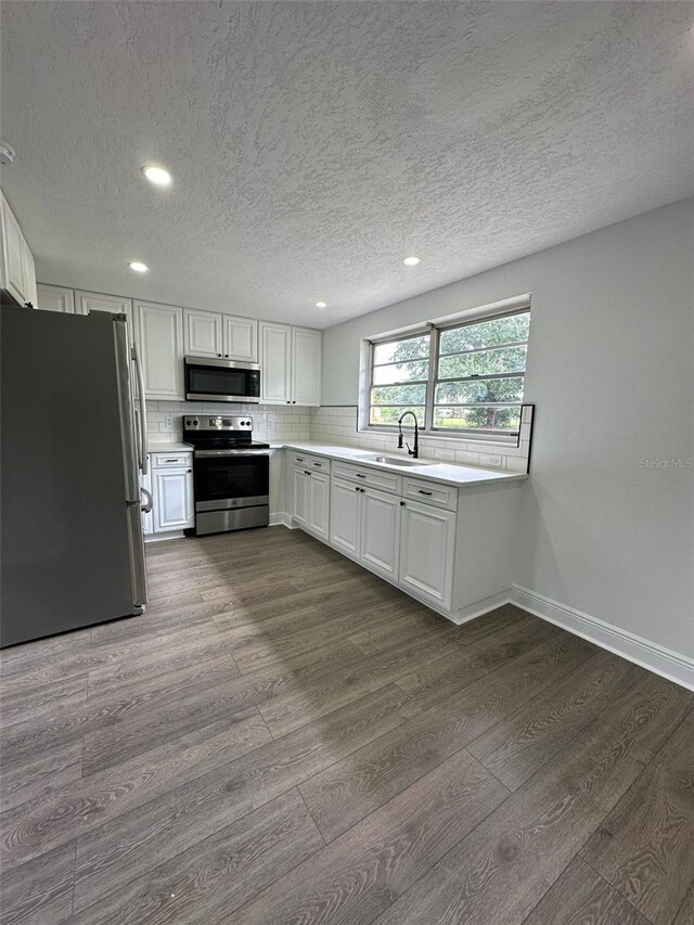 kitchen featuring wood-type flooring, appliances with stainless steel finishes, white cabinets, and tasteful backsplash