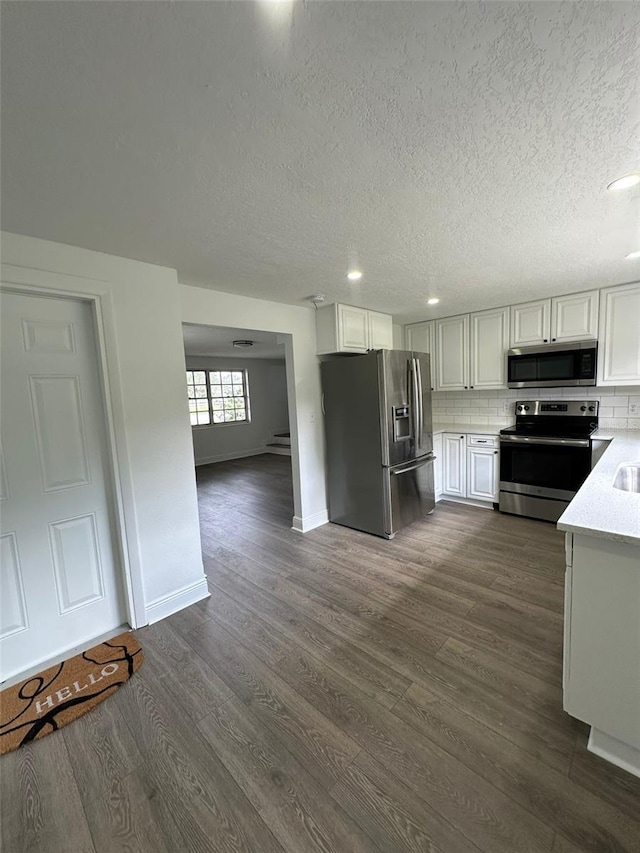 kitchen with appliances with stainless steel finishes, white cabinetry, dark hardwood / wood-style floors, tasteful backsplash, and a textured ceiling