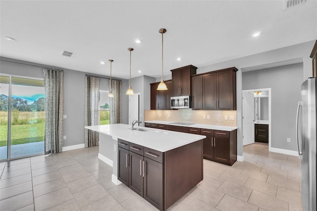 kitchen with tasteful backsplash, hanging light fixtures, stainless steel appliances, dark brown cabinetry, and a kitchen island with sink