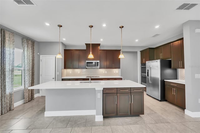 kitchen with a center island with sink, appliances with stainless steel finishes, dark brown cabinetry, and decorative light fixtures