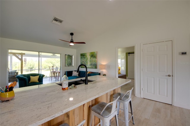 kitchen with light hardwood / wood-style flooring, a kitchen bar, light stone counters, sink, and ceiling fan