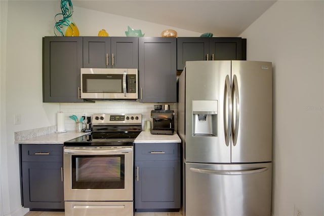 kitchen with appliances with stainless steel finishes, light stone counters, backsplash, and vaulted ceiling