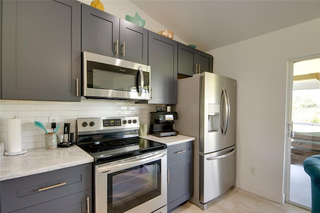 kitchen featuring vaulted ceiling, appliances with stainless steel finishes, light hardwood / wood-style floors, decorative backsplash, and light stone counters