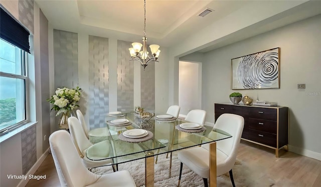 dining space featuring a notable chandelier, a raised ceiling, and light wood-type flooring