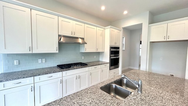 kitchen with white cabinets, black gas stovetop, dark stone counters, double oven, and sink