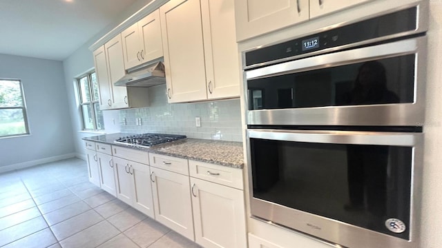 kitchen featuring appliances with stainless steel finishes, backsplash, white cabinets, light stone counters, and light tile patterned floors