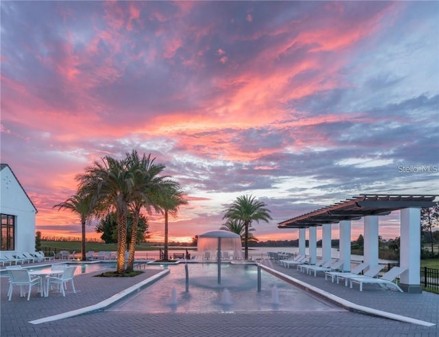 pool at dusk with a patio area, pool water feature, and a pergola