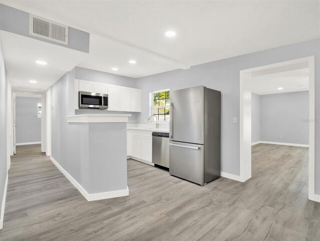 kitchen featuring appliances with stainless steel finishes, white cabinetry, light hardwood / wood-style flooring, and sink