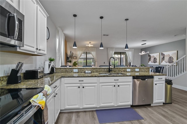 kitchen with appliances with stainless steel finishes, dark stone countertops, white cabinetry, and sink