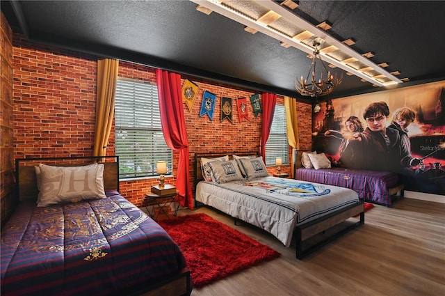 bedroom featuring a chandelier, a textured ceiling, brick wall, and hardwood / wood-style floors