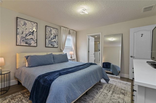 bedroom featuring a textured ceiling, ensuite bathroom, and dark hardwood / wood-style flooring