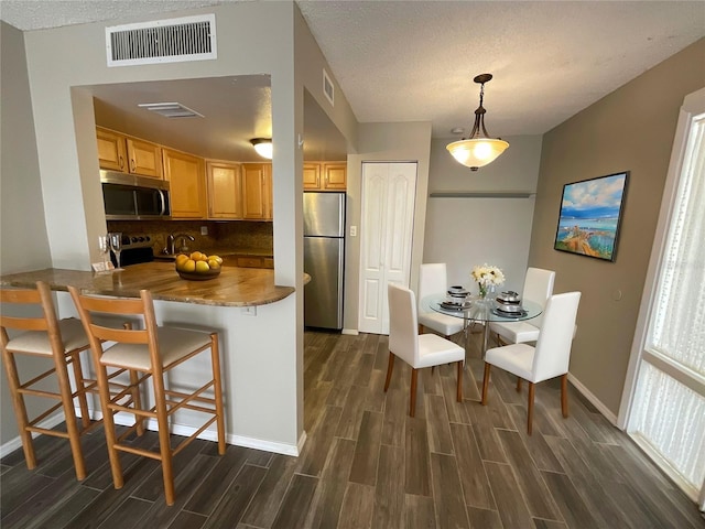 kitchen with stainless steel appliances, a kitchen breakfast bar, dark hardwood / wood-style floors, kitchen peninsula, and light brown cabinetry