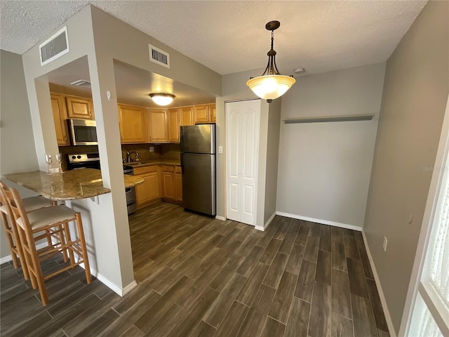 kitchen with light brown cabinets, dark wood-type flooring, kitchen peninsula, a textured ceiling, and appliances with stainless steel finishes