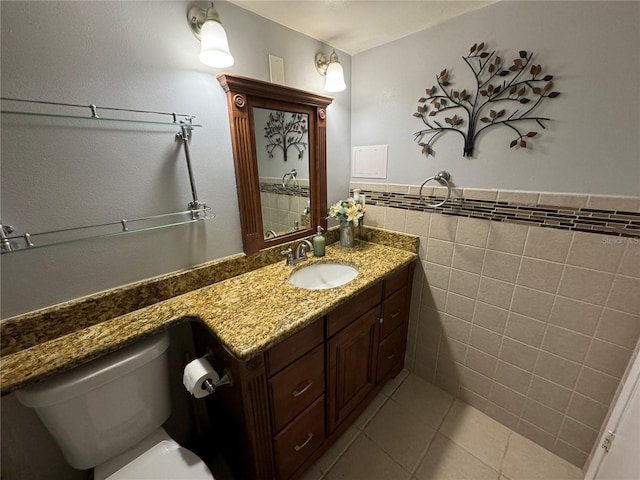 bathroom with toilet, vanity, tile patterned floors, and tile walls