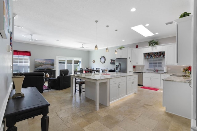 kitchen with a kitchen island, appliances with stainless steel finishes, decorative light fixtures, white cabinets, and ceiling fan