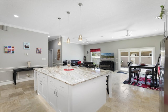 kitchen with a kitchen island, stainless steel refrigerator, white cabinets, hanging light fixtures, and light stone countertops