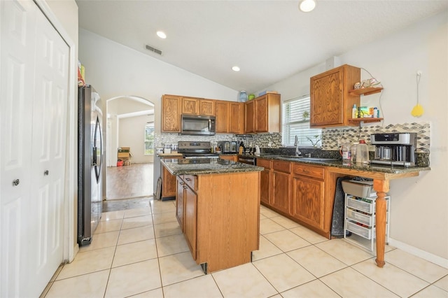 kitchen with appliances with stainless steel finishes, vaulted ceiling, light tile patterned floors, a center island, and dark stone counters