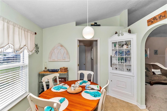 dining area with a textured ceiling, light colored carpet, and lofted ceiling