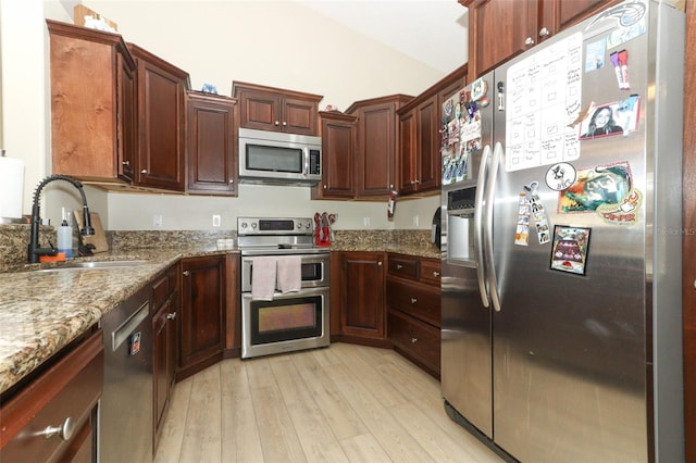 kitchen featuring light stone counters, stainless steel appliances, sink, and light hardwood / wood-style floors