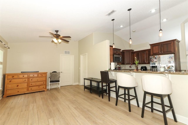 kitchen with decorative light fixtures, appliances with stainless steel finishes, stone countertops, and light hardwood / wood-style flooring