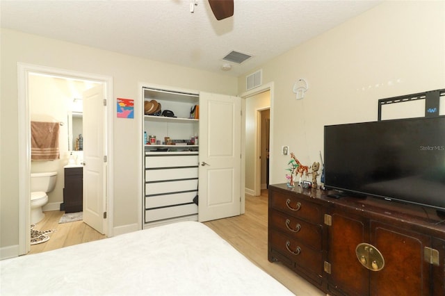 bedroom with light wood-type flooring, a textured ceiling, connected bathroom, and ceiling fan