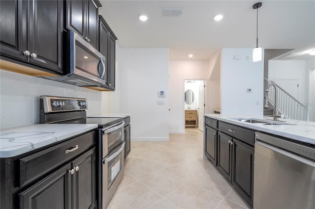 kitchen with decorative light fixtures, light stone countertops, sink, and appliances with stainless steel finishes