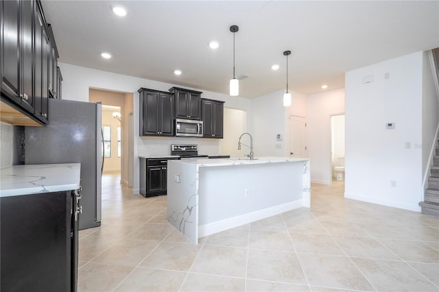 kitchen featuring a center island with sink, light tile patterned floors, decorative light fixtures, and appliances with stainless steel finishes