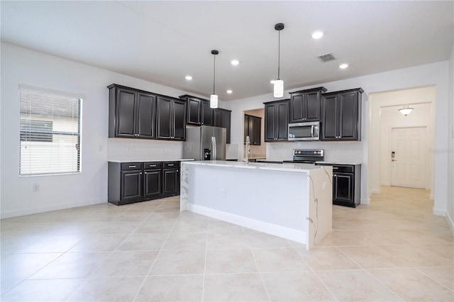 kitchen with decorative light fixtures, stainless steel appliances, a center island with sink, and light tile patterned flooring