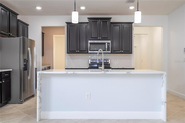 kitchen with tasteful backsplash, a center island with sink, hanging light fixtures, and appliances with stainless steel finishes