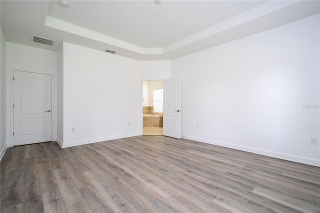 unfurnished room with light wood-type flooring and a tray ceiling