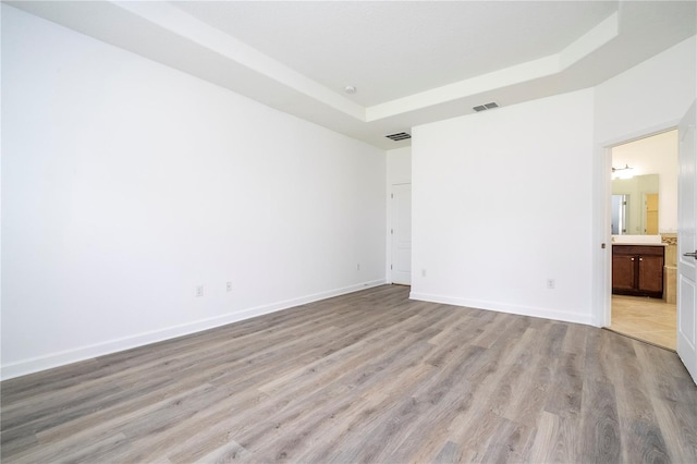 unfurnished room with light wood-type flooring and a raised ceiling