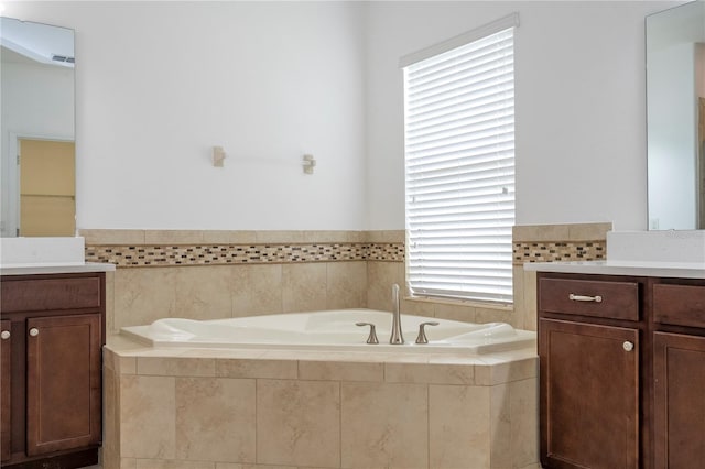 bathroom featuring vanity, a healthy amount of sunlight, and a relaxing tiled tub