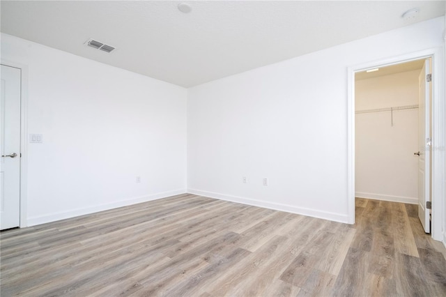 unfurnished bedroom with a walk in closet, a closet, and light wood-type flooring