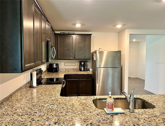 kitchen featuring dark brown cabinets, hardwood / wood-style flooring, stainless steel appliances, and light stone countertops