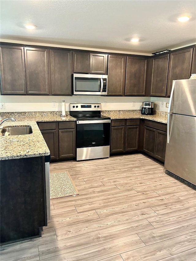 kitchen featuring light wood-type flooring, appliances with stainless steel finishes, light stone counters, sink, and dark brown cabinetry