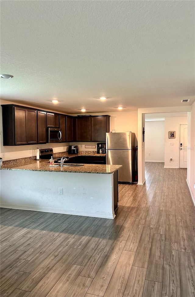 kitchen with stainless steel appliances, dark stone countertops, light wood-type flooring, and dark brown cabinets