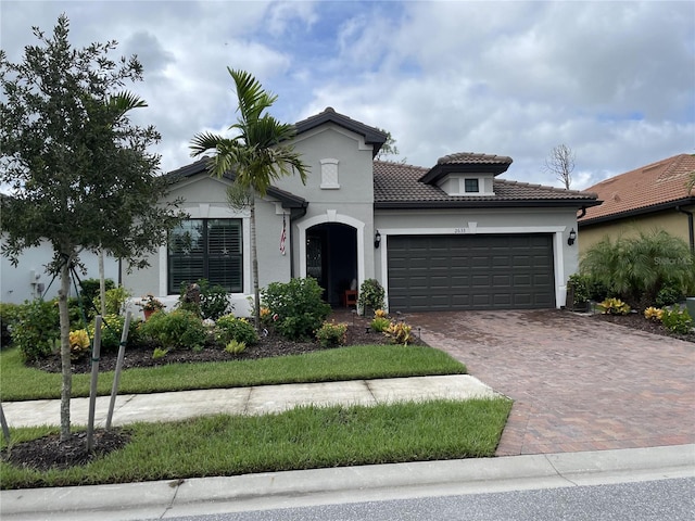 mediterranean / spanish-style house featuring a garage, stucco siding, decorative driveway, and a tiled roof