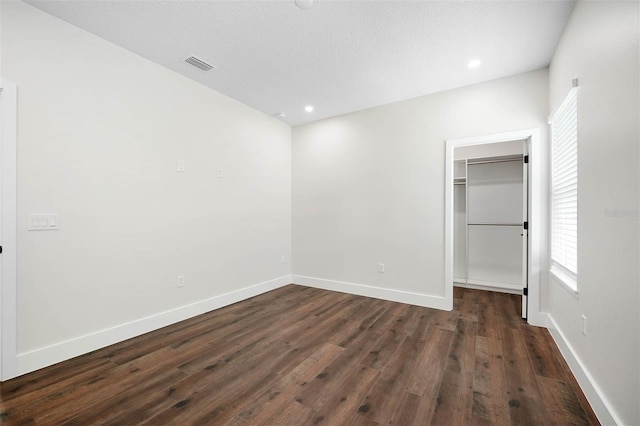 unfurnished bedroom with a textured ceiling, a closet, a walk in closet, and dark hardwood / wood-style flooring