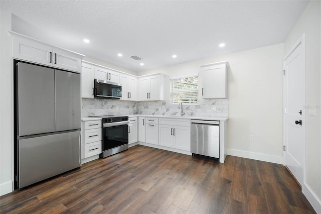 kitchen with tasteful backsplash, dark wood-type flooring, sink, white cabinets, and appliances with stainless steel finishes