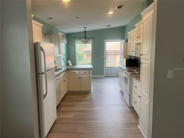 kitchen featuring kitchen peninsula, vaulted ceiling, light hardwood / wood-style floors, a notable chandelier, and white appliances