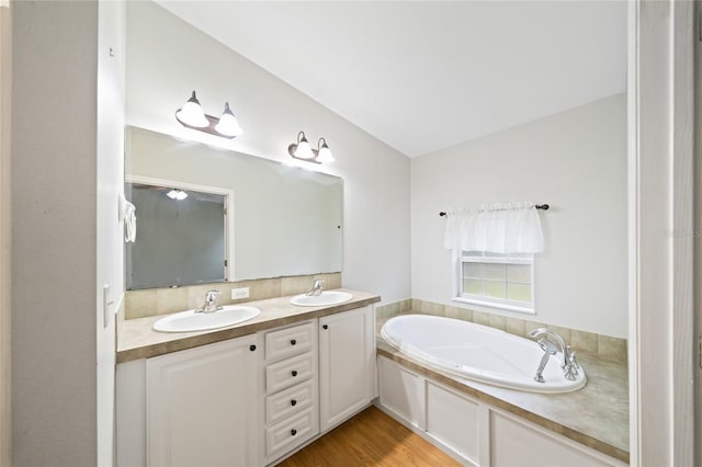 bathroom with vanity, a tub to relax in, vaulted ceiling, and hardwood / wood-style floors