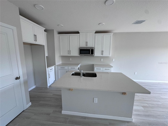 kitchen featuring white cabinetry, a center island with sink, and sink